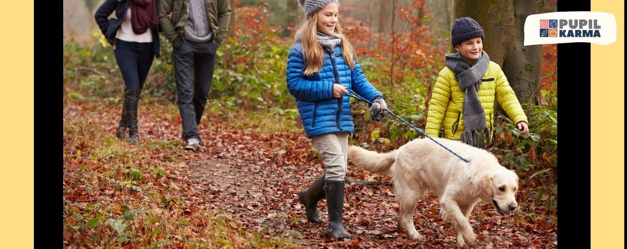 Zdjęcie rodziny spacerującej z psem na smyczy. Dzieci z przodu, rodzice z tyłu, Jesień w parku lub lesie. Po bokach kolorowe psay i logotyp pupilkarma.